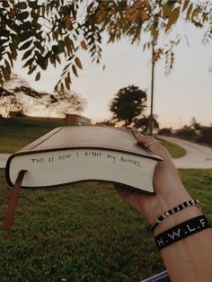 a hand holding an open book with writing on it in front of a grassy field