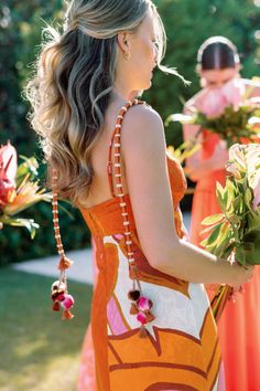 a woman in an orange dress is holding flowers and looking at another woman with her back to the camera