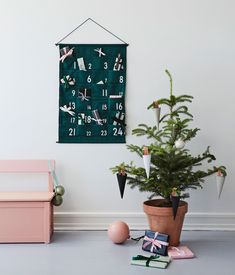 a small christmas tree in a pot next to a wall hanging with calendars on it