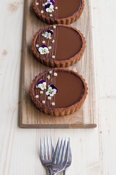 three chocolate tarts with white flowers on them and a fork next to the tart