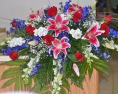 an arrangement of red, white and blue flowers in a wooden box with greenery