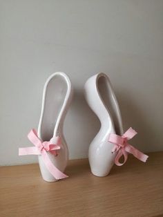 two white vases with pink bows are sitting on a wooden table next to each other