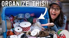 a woman pointing at an open blue container filled with ribbon and other items that are labeled organize this