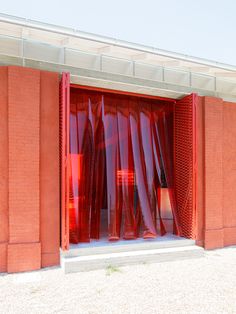 an open red door in front of a brick building with plastic coverings on it