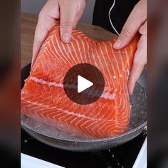 a person is holding a piece of salmon in a frying pan