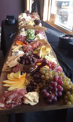 a long wooden table topped with lots of different types of cheeses and meats