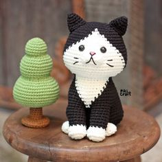 a crocheted black and white cat sitting next to a small tree