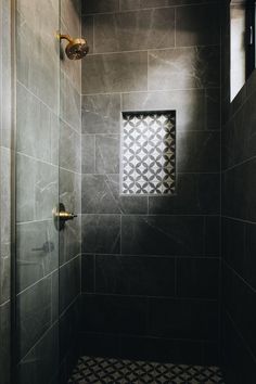 a walk in shower sitting next to a tiled wall and floor covered in black tiles