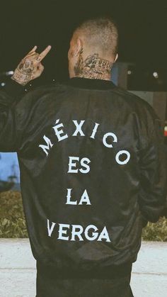 a man wearing a black jacket with mexican writing on it and pointing to the side