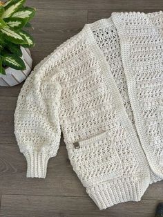 a white knitted sweater sitting on top of a wooden floor next to a potted plant