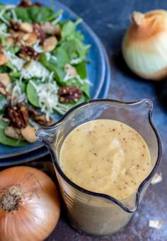 a salad with dressing in a pitcher next to an onion and garlic on a plate