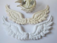 three angel wings and a mirror on a white table top with the reflection of an angel in it