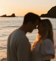 a man and woman standing next to each other in front of the ocean at sunset