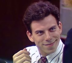 a man with curly hair wearing a white shirt and red tie smiling at the camera