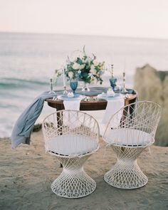 two white chairs sitting on top of a sandy beach next to an umbrella and table