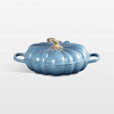 a blue pumpkin shaped casserole sitting on top of a white surface with a gold handle