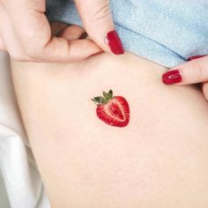 a woman's stomach with a strawberry tattoo on it and a red nail polish