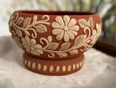 two brown and white flower pots sitting on top of a cloth covered table next to a potted plant