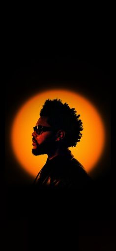 the silhouette of a man wearing sunglasses in front of an orange light