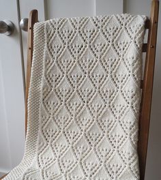 a white knitted blanket sitting on top of a wooden chair next to a door