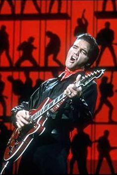 the man is playing his guitar in front of some people and red lighting on stage