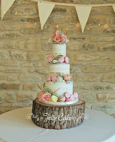 a three tiered cake with pink flowers on top is sitting on a tree stump