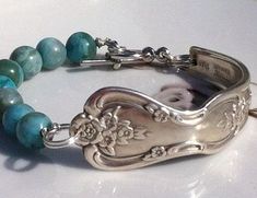 a silver bracelet with blue and green beads on it's side, sitting on a white surface