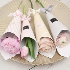 three paper cones with flowers in them sitting on a plate next to some pink tulips