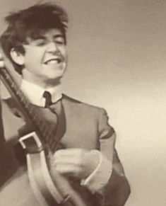 a young man holding a guitar in his right hand and smiling at the camera while wearing a suit