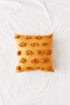 a yellow pillow with orange flowers on it sitting on a white bedding sheet, top view