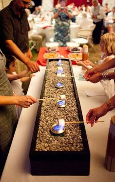 people standing around a long table with candles on it and bowls in the middle, surrounded by other people