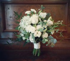 a bouquet of white flowers sitting on top of a wooden table next to a wall