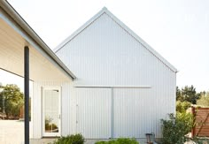 a white building with a door and some plants in front of it by the side of the house