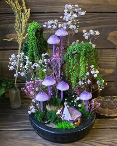 an arrangement of purple mushrooms and other plants in a black bowl on a wooden table