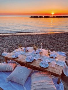 a table set up on the beach for an outdoor dinner with candles, plates and napkins