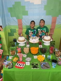 two young boys sitting in front of a table with cake and candy on it at a minecraft themed birthday party