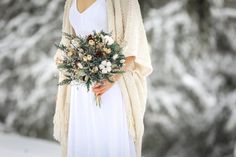 a woman wearing a white dress holding a bouquet of flowers in her hand and a cardigan over her shoulder