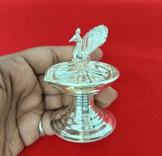 a hand is holding a small silver candle holder on a red surface with a white background