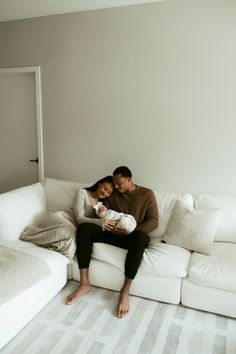 a man and woman are sitting on a white couch with a baby in their lap