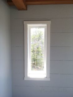 a window in the corner of a room with white painted walls and wood beams on the ceiling