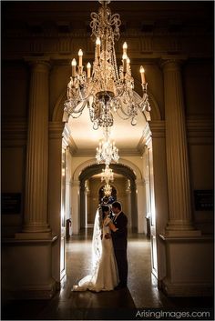 a bride and groom standing under a chandelier in an ornate hallway at night