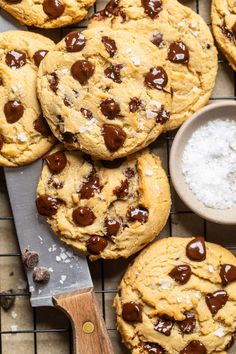 chocolate chip cookies on a cooling rack next to a bowl of sea salt and a knife