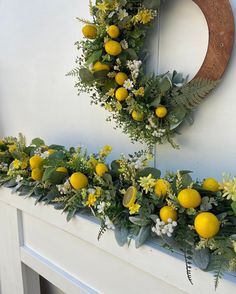 a wreath with lemons and greenery hanging on the mantle