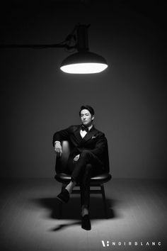 a man in a tuxedo sitting on a chair under a light fixture with his legs crossed