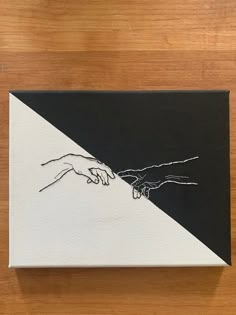 two hands touching each other over a black and white painting on a wooden table top