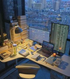 an office desk with two computers on top of it and a view of the city