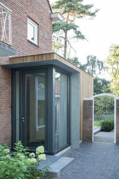 a brick building with an open door and glass windows on the outside, surrounded by greenery