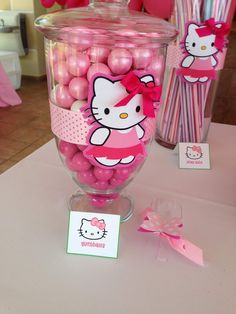 hello kitty candy in a glass container on a table with pink balls and paper tags