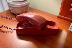 a red telephone sitting on top of a wooden table next to plates and bowls in the background