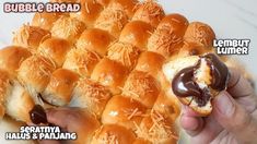 a person holding a hot dog bun in front of a pile of rolls with chocolate frosting on them